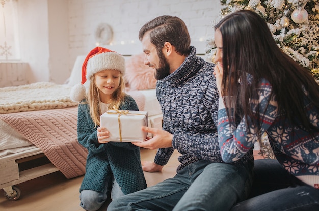 Frohe Weihnachten und schöne Feiertage Fröhliche Mutter, Vater und ihr süßes Tochtermädchen tauschen Geschenke aus.