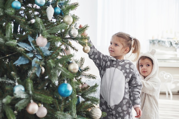 Frohe Weihnachten und schöne Feiertage! Junge Mädchen, die beim Verzieren des Weihnachtsbaums helfen und etwas Weihnachtsflitter in ihrer Hand halten