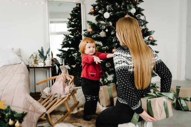 Frohe Weihnachten und schöne Feiertage Mama gibt ihrer Tochter in der Nähe des Weihnachtsbaums ein Geschenk