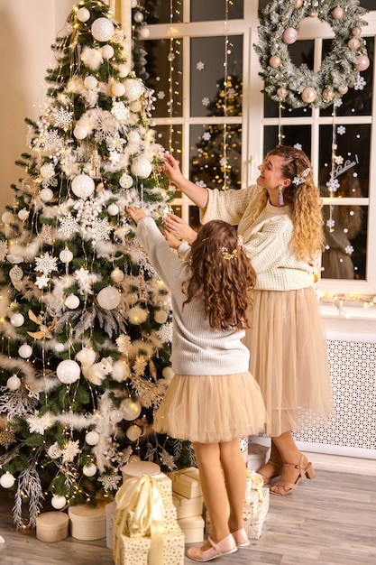 Frohe Weihnachten und schöne Feiertage. Mutter und Tochter, die Weihnachtsbaum schmücken. Festlicher Abend