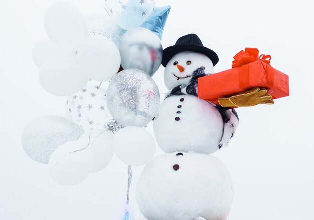 Frohe Winterzeit. Schneemann mit Ballons und Geschenk. Schneemann mit Hut, Schal, Handschuhen.