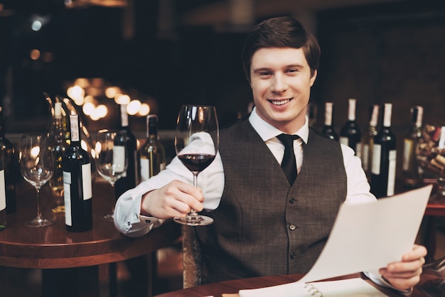 Froher eleganter junger Mann hält Glas Rotwein.