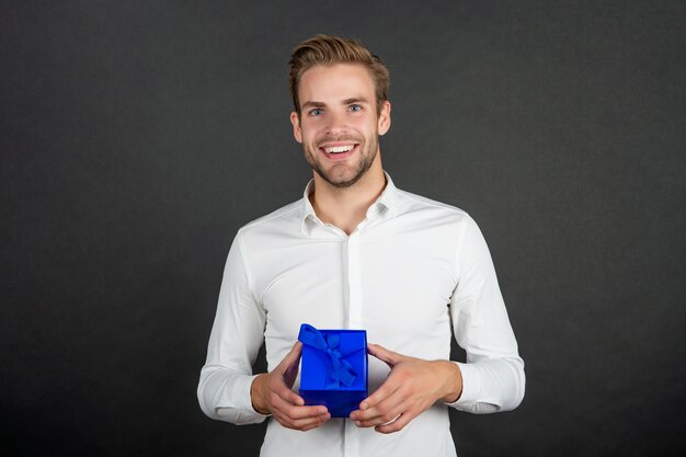 Froher eleganter Kerl im sachlichen Anzug hält Valentinstagsgeschenk, sei mein Valentinsgruß