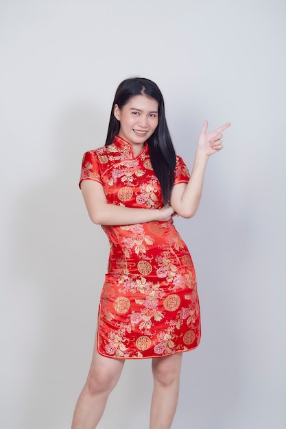 Frohes chinesisches Neujahr. Schöne asiatische Frau, die traditionelles Cheongsam-Qipao-Kleid mit Glückwunschgeste auf hellgrauer Oberfläche mit Kopienraum trägt