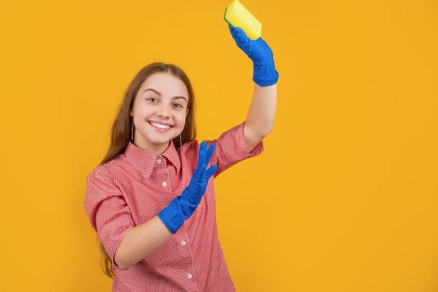 Frohes Kind in Gummihandschuhen mit Schwamm auf gelbem Hintergrund