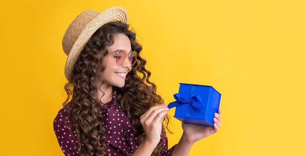 Frohes Kind mit lockigem Haar hält Geschenkbox auf gelbem Hintergrund