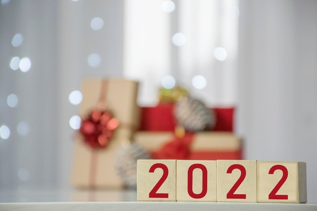 Frohes Neues Jahr 2022 auf Holzwürfelblöcken mit Geschenkboxen und verschwommenen Bokeh-Lichtern auf dem Hintergrund. Grußkarte für Winterferien und Weihnachten.