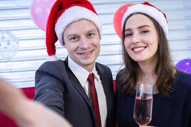 Frohes neues Jahr 2022 Konzept, Selfie des glücklichen Paares, das das Champagnerglas in der Weihnachts- und Silvesterparty hält Weihnachtsbaumhintergrund nach Beendigung der Geschäftsarbeiten