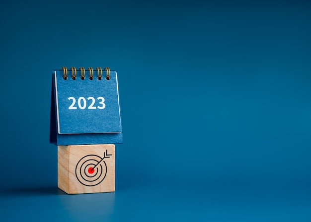 Frohes neues Jahr 2023 Hintergrund 2023 Zahlen Jahr auf kleinem Tischkalender auf Holzwürfelblock mit Zielsymbol isoliert auf blauem Hintergrund mit Kopierraum minimalistisch Bereit für neue Ziele