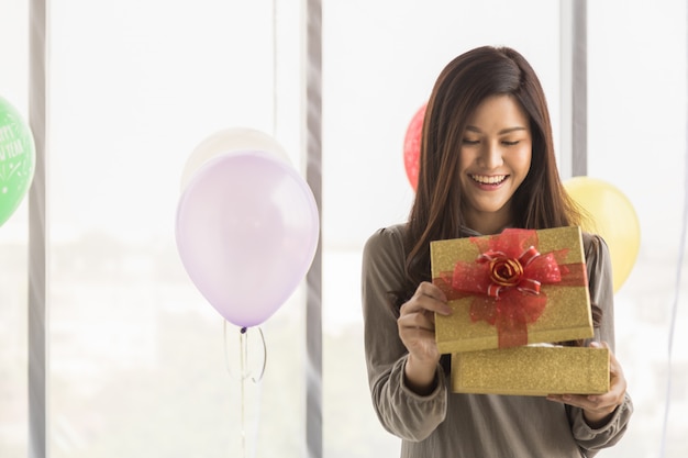 Frohes neues Jahr und Urlaub saisonale Konzept. Porträt der schönen asiatischen jungen Frau, die mit Geschenkbox mit buntem Ballon lächelt und überrascht