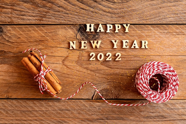 Frohes neues Jahr-Zitat mit Holzbuchstaben, verziert mit Zimtstangen und roter und weißer Schnur. Festlicher Hintergrund des neuen Jahres