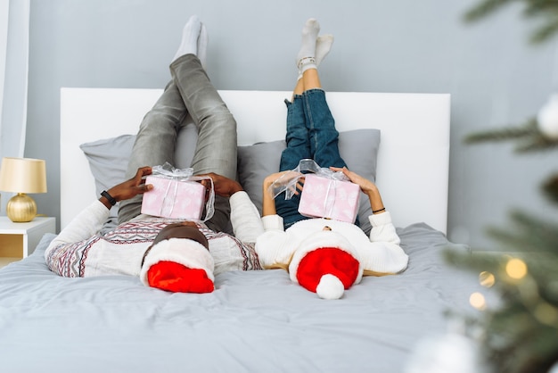 Frohes paar zusammen im bett am weihnachtsmorgen. kaukasische frau und afroamerikaner feiern zusammen weihnachten