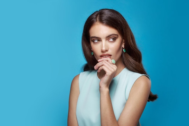 Frontalporträt einer jungen Frau in hellblauem Kleid, mit eleganten Accessoires, seitlicher Blick, isolierter blauer Hintergrund.