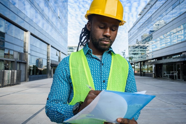 Frontansicht afrikanischer Ethnie männlicher Bauingenieur denkt und macht Notizen auf einer blauen Mappe