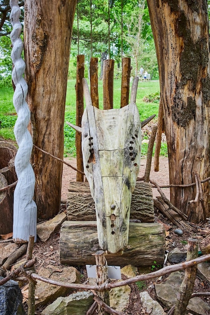Frontansicht eines hölzernen Drachenkopfes auf Holzstämmen neben einem hohen weißen Einhornhorn