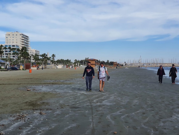 Foto frontansicht von menschen, die am strand gegen den himmel spazieren gehen