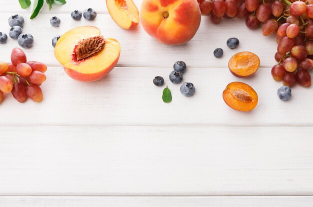 Fronteira de frutas da estação e bagas em fundo de madeira. uvas, pêssegos, mirtilos e ameixas na vista superior da mesa branca com espaço de cópia. refeições orgânicas frescas e conceito de alimentação saudável