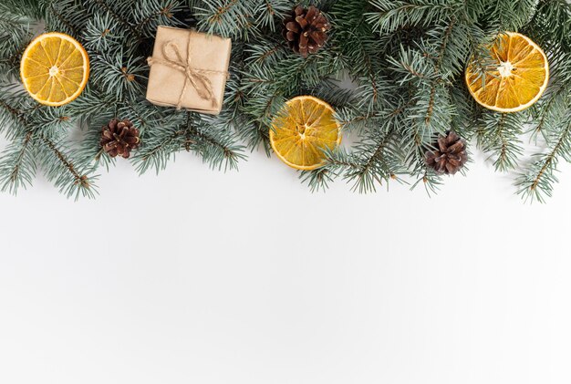 Fronteira de Natal com galhos de pinheiro, cones, presentes e laranjas secas em um fundo branco.