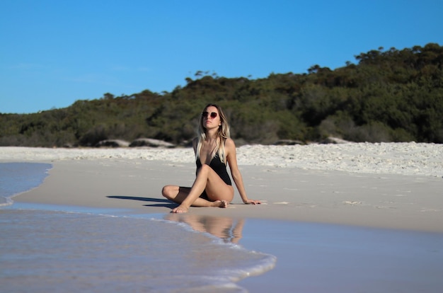 Frontporträt einer jungen Frau im schwarzen Bikini, die am Strand sitzt