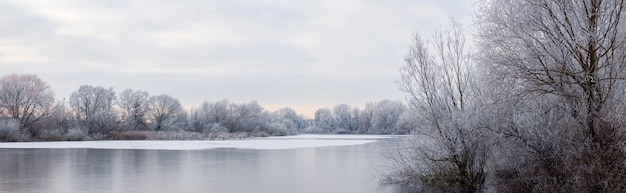 Frostbedeckte Bäume am Ufer eines vereisten Flusses morgens bei Sonnenaufgang