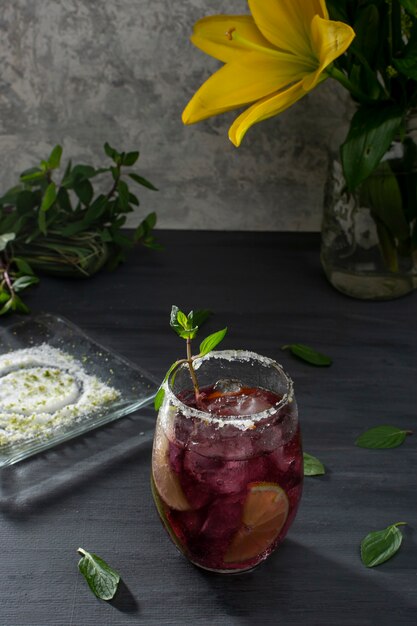 Frostiges Getränk mit Eis und Zitronenscheiben auf einem grauen Tisch und einer Vase mit gelben Blumen