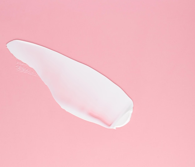 Foto frotis de crema blanca para la cara y el cuerpo sobre un fondo rosa