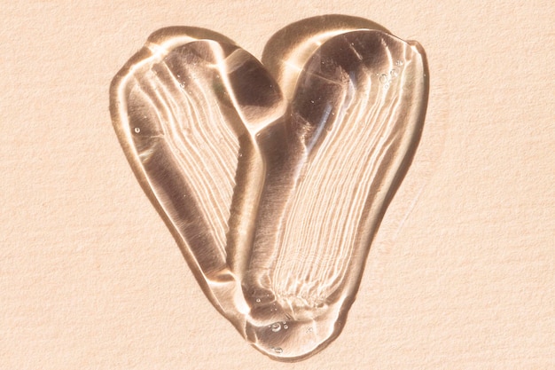 Frotis de un producto cosmético líquido transparente sobre un fondo beige en forma de corazón