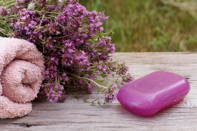 Frotteehandtuch für Badprozeduren mit Thymianblüten und Seife auf Holzbrettern