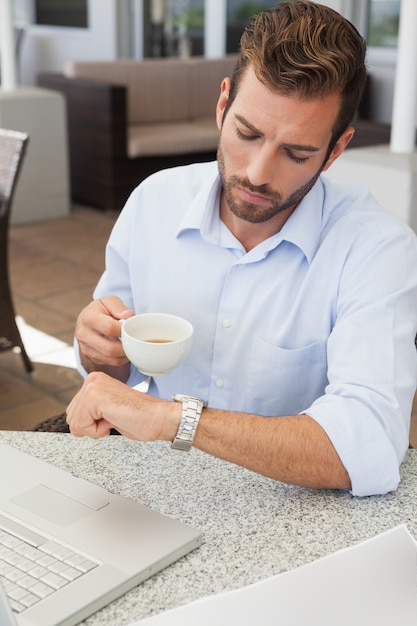 Frowning jovem empresário verificando tempo segurando copo de café