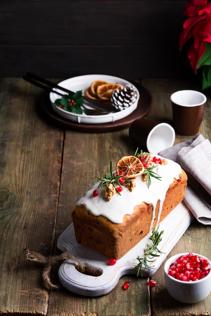 Fruchtkuchen bestäubt mit Zuckerglasur, Nüssen, Kerngranatapfel und trockenem orange altem hölzernem. Weihnachts- und Winterferien hausgemachten Kuchen