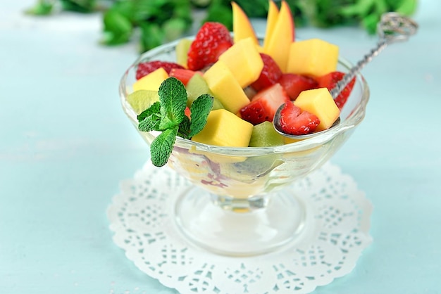 Fruchtsalat in einer Glasschüssel mit Minze auf farbigem Holzhintergrund