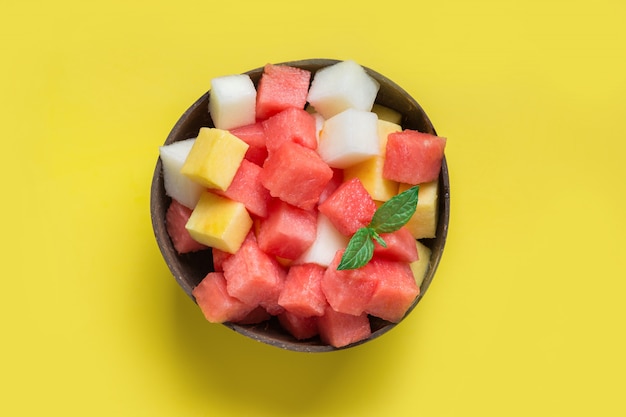 Fruchtsalat von Wassermelone, Melone und Mango in der Kokosnussschale auf gelbem Hintergrund. Von oben betrachten.