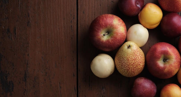 Früchte auf einem alten Holztisch Äpfel Birnen Pflaumen Aprikosen auf dunkelrotem Hintergrund