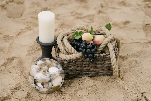 Früchte in einem Korb, eine Kerze, Meeressteine in einer Glasvase, Dekor für ein romantisches Abendessen am Meer oder Ozean.