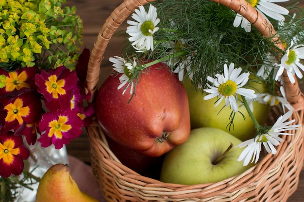 Früchte in einem Weidenkorb auf einem hölzernen Hintergrund mit Blumen in einer Vase Das Konzept eines Dorfes Saubere Ökologie