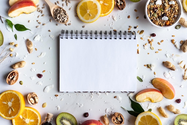 Früchte, Nüsse, Granola-Samen und ein leeres, leeres Notizbuch auf weißem Hintergrund