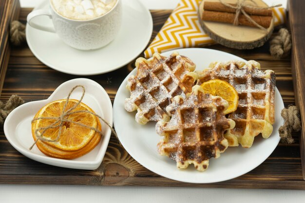 Frühes Frühstückskaffee mit Marshmallows und einer Zimtstange und belgischen Waffeln liegt auf einem Holztablett