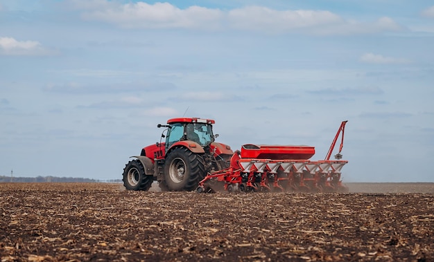 Frühjahrsaussaat Bauer mit einem Traktor sät Maissamen auf seinem Feld Anpflanzen von Mais mit gezogenem Pflanzer Landwirtschaftliche Aussaat Das Konzept der Landwirtschaft und der landwirtschaftlichen Maschinen