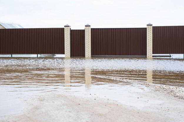 Frühjahrshochwasser in ländlichen Gebieten, Überschwemmung des Flusses, Überschwemmung von Hausgrundstücken hinter dem Zaun, Elemente nach der Schneeschmelze und starken Regenfällen