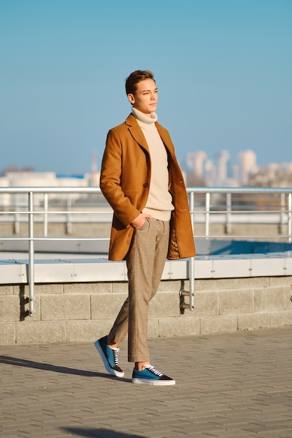 Frühling - Herbst-Outfit. Straßenmode. Junger Mann in karierter Hose, Pullover und Wollmantel.