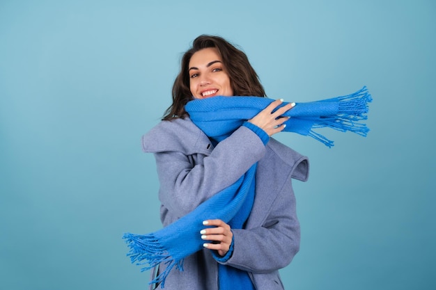 Frühlings-Herbst-Porträt einer Frau in einem blauen Strickpullover, Schal und grauem Mantel, die fröhlich posiert, lächelnd, in Erwartung des Frühlings