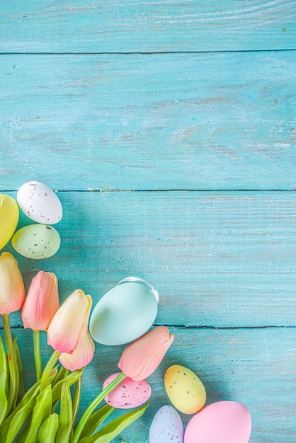 Frühlings- und osterferienhintergrund mit tulpenblumen, bunte pastelleier auf blauer tischoberansicht. frohe ostern-grußkarte.