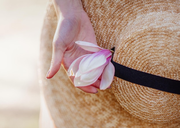 Frühlingsblüte Offene Blende mit leichter Unschärfe und Beleuchtung Eine Frauenhand mit einer Blume auf dem Hintergrund eines Strohhutes mit großer Krempe Frühling