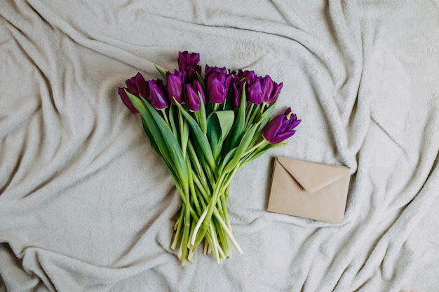 Frühlingsblumen, Bündel lila Tulpen und Umschlag auf beigem Plaid.