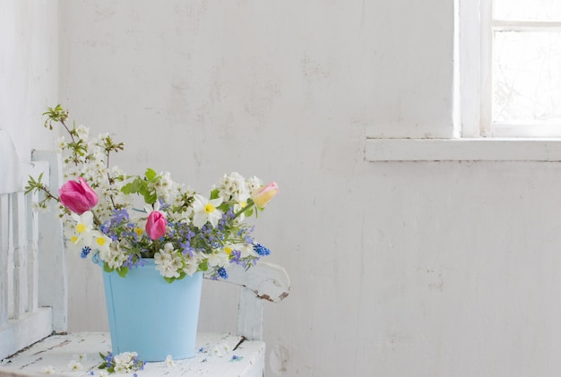 Frühlingsblumen im Weinleseweißinnenraum mit alter Holzbank