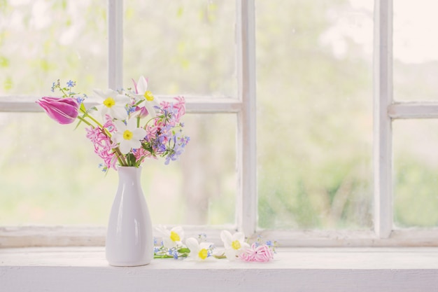 Frühlingsblumen in der weißen vase auf altem fensterbrett