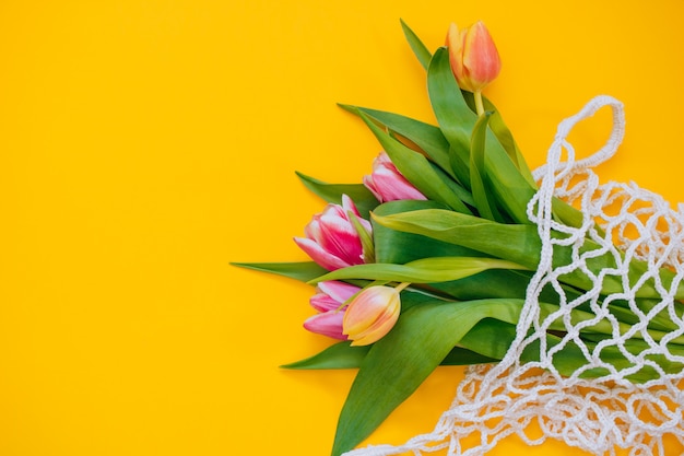 Frühlingsblumenstrauß von mehrfarbigen Tulpen in der eco Tasche auf einem gelben Hintergrund. Kopieren sie platz, flach legen hintergrund.