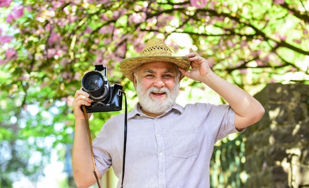 Frühlingsferien. Reisefoto. Fotograf im blühenden Garten. Freizeit genießen. Reisen und Tourismus. Schönheit einfangen. Glücklicher Großvater. Älterer Mann hält professionelle Kamera. Reise in den Ruhestand.