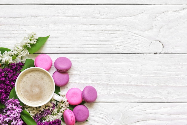 Frühlingsfliederblumenstrauß mit Macarons und Cappuccino-Tasse auf weißem Holztisch