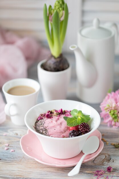Frühlingsfrühstück mit einer Tasse Kaffee auf einem hölzernen Hintergrund. Müsli mit Erdbeeren, Nüssen und Milch.